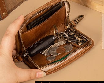 May include: Open brown leather key wallet with a zipper, holding keys, coins, and a car key. The wallet is open, revealing a card slot and a key ring. The text at the bottom reads: "Simultaneously store six keys and car keys without pressure."