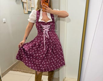 May include: A burgundy dirndl dress with a floral pattern and a white blouse. The dress features a laced bodice and a flared skirt. The outfit is paired with brown knee-high boots. The dress is a traditional German garment.