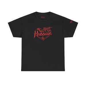 Puede incluir: Camiseta negra con un diseño rojo en forma de corazón. El diseño incluye el texto "My Heart Beats for Hussain" en una fuente estilizada, con una línea de latido del corazón. La camiseta tiene mangas cortas y cuello redondo.