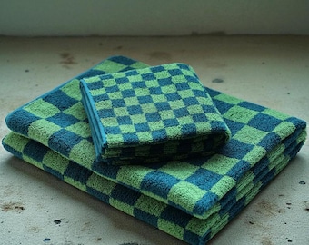 May include: A stack of three checkered towels in shades of green and blue. The towels are folded and stacked on top of each other, with the smallest towel on top. The pattern is a classic checkerboard design.