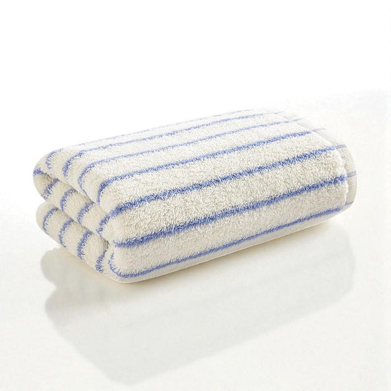 May include: Folded white towel with blue horizontal stripes. The towel is made of a soft, absorbent material and is folded neatly. The stripes are evenly spaced across the width of the towel.