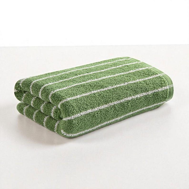 May include: Folded green towel with white horizontal stripes. The towel is made of a soft, absorbent material, perfect for use in a bathroom or spa. The simple design and color scheme make it a versatile addition to any home.