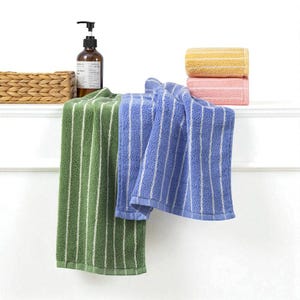 May include: A display of striped bath towels in shades of green and blue, with a stack of rolled towels in yellow and pink. A brown soap dispenser and a woven basket are also visible on a white shelf. The towels have white stripes.