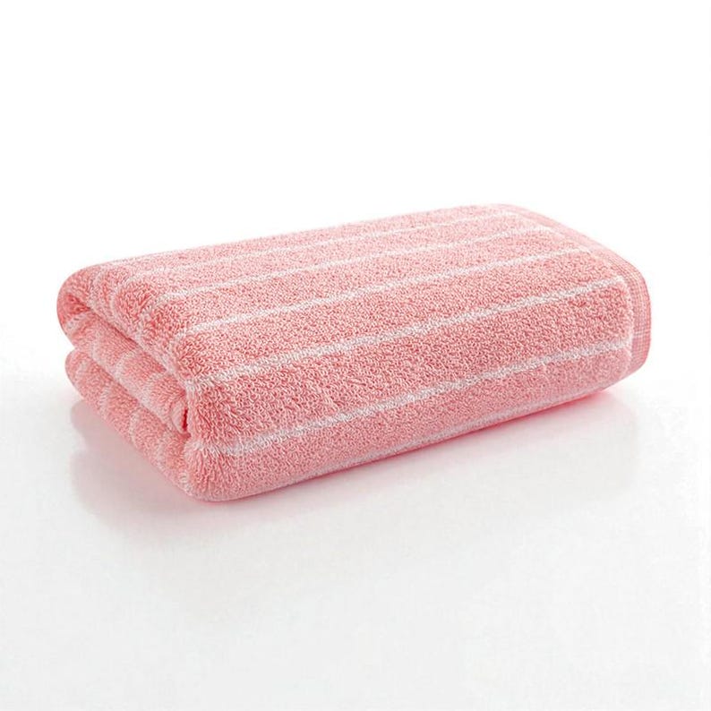 May include: Folded pink bath towel with white horizontal stripes. The towel is made of a soft, absorbent material, perfect for use in a bathroom or spa setting. The stripes add a simple, yet elegant design.