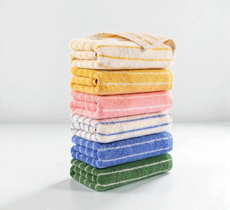May include: A stack of seven folded towels in various colors: cream with yellow stripes, yellow, pink, white with blue stripes, blue, and green. The towels are neatly arranged, showcasing a range of hues and striped patterns. The towels are made of a soft, absorbent material.