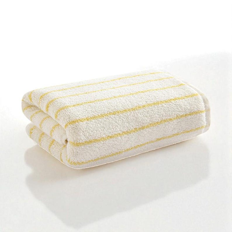May include: Folded white towel with yellow horizontal stripes. The towel is made of a soft, absorbent material and is folded neatly. The stripes are evenly spaced across the towel.