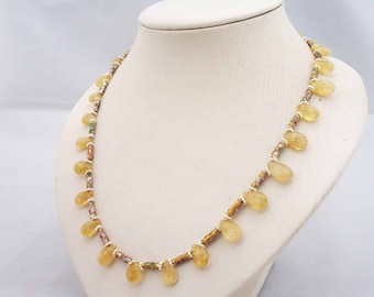 May include: A delicate necklace featuring teardrop-shaped yellow gemstones. The necklace is strung with small, silver-colored beads and interspersed with sections of smaller, colorful beads. The necklace is displayed on a white mannequin bust.