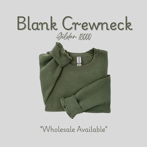 May include: An olive green blank crewneck sweatshirt, folded neatly. The text "Blank Crewneck" and "Gildan 18000" are displayed above the sweatshirt. The words "Wholesale Available" are at the bottom.