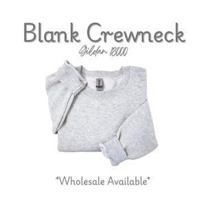 K&ouml;nnte beinhalten: Ein hellgraues, leeres Crewneck-Sweatshirt, ordentlich gefaltet. Der Text "Blank Crewneck" steht &uuml;ber dem Sweatshirt, darunter "Gildan 18000". Die Worte "Wholesale Available" stehen unten.