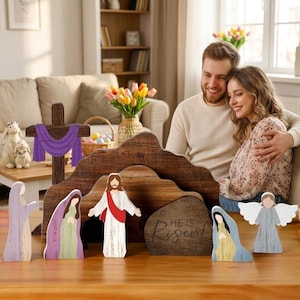 Può includere: Scena pasquale in legno con figure di Gesù, un angelo e altri personaggi biblici. Sono presenti anche una croce di legno con un drappo viola e un sepolcro di legno con la scritta "He is Risen". La scena è ambientata su un tavolo di legno.