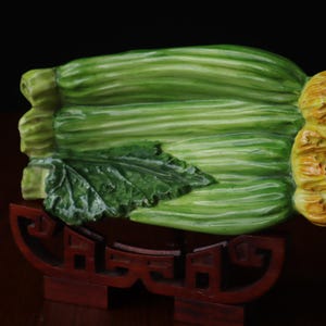Peut inclure: Une sculpture décorative verte et jaune d'un légume, peut-être un chou ou une plante à feuilles similaire. La sculpture repose sur un support en bois rouge foncé. Le légume présente des textures détaillées et un aspect réaliste.