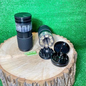 May include: Black and clear herb grinder with multiple components, including a cylindrical body, a clear chamber, and a lid. The grinder is displayed on a wooden surface with the text "WISE FUME" and "wisefume.com".