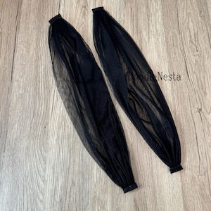 Puede incluir: Dos mangas negras transparentes con puños elásticos y tela fruncida. Las mangas están hechas de un material ligero y transparente. Las mangas están sobre una superficie de madera.