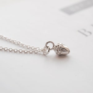 May include: A silver necklace featuring a small acorn charm. The chain is delicate and the acorn is detailed.