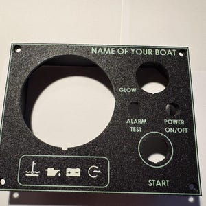 May include: Black boat control panel with the text "NAME OF YOUR BOAT", "GLOW", "ALARM TEST", "POWER ON/OFF", and "START". Features indicator symbols and circular cutouts for gauges and switches.