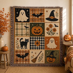 May include: A woven throw blanket featuring a grid of twelve squares with Halloween motifs including ghosts, a jack-o'-lantern, a black cat, bats, a witch hat, a broom, and flowers. The design uses a palette of black, orange, and cream colors.