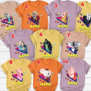 May include: A collection of ten colorful t-shirts featuring cartoon characters. Each shirt has a unique character design within a geometric shape, with the word "NAME" printed below. The shirts are in various colors, including tan, orange, purple, and yellow.