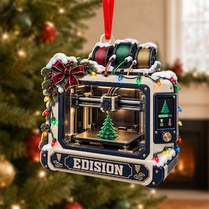 May include: A 3D printer Christmas ornament featuring a cream and navy frame with the text EDISION. It is decorated with a red bow, holly, and colorful string lights. The printer is creating a green tree, with red, green, and gold filament spools on top.