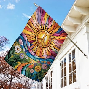 May include: A colorful outdoor flag featuring a stained-glass design with a vibrant sun and peace symbol at the center. The flag also displays a field of flowers and a flowing river, with a blue sky background.