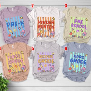 May include: A collection of six short-sleeved t-shirts with school-themed designs. Each shirt features a grade level, a pencil, an apple, a backpack, and the text "MRS. ALICE". The shirts are in various colors.