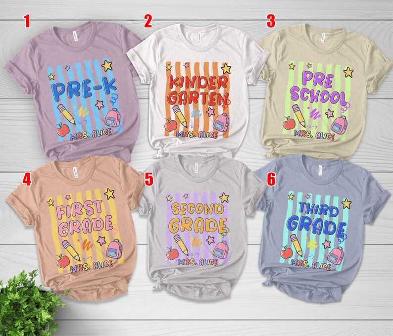 May include: A collection of six short-sleeved t-shirts with school-themed designs. Each shirt features a grade level, a pencil, an apple, a backpack, and the text "MRS. ALICE". The shirts are in various colors.