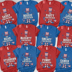May include: A selection of red and blue t-shirts with patriotic designs. Each shirt features an Uncle Sam hat graphic and a phrase such as "The Sassy Firecracker", "The Bougie Firecracker", or "The Party Firecracker", with American flag accents.