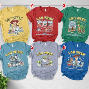 May include: A collection of six short-sleeved t-shirts in various colors, each featuring a "LAB WEEK" graphic with cartoon characters and the year 2026. The shirts are yellow, red, green, blue, gray, and navy blue.