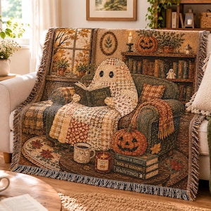 May include: A woven throw blanket featuring a ghost reading a book titled Ghost Stories on a sofa. The scene includes a jack-o'-lantern, a mug with a ghost face, a candle, and a stack of books labeled Spirits & Spells, Book of Shadows, and Hauntings.