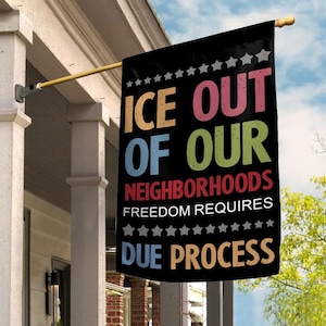 May include: Black flag with the text "ICE OUT OF OUR NEIGHBORHOODS FREEDOM REQUIRES DUE PROCESS" in various colors. The flag is hanging from a gold-colored pole attached to a white porch.