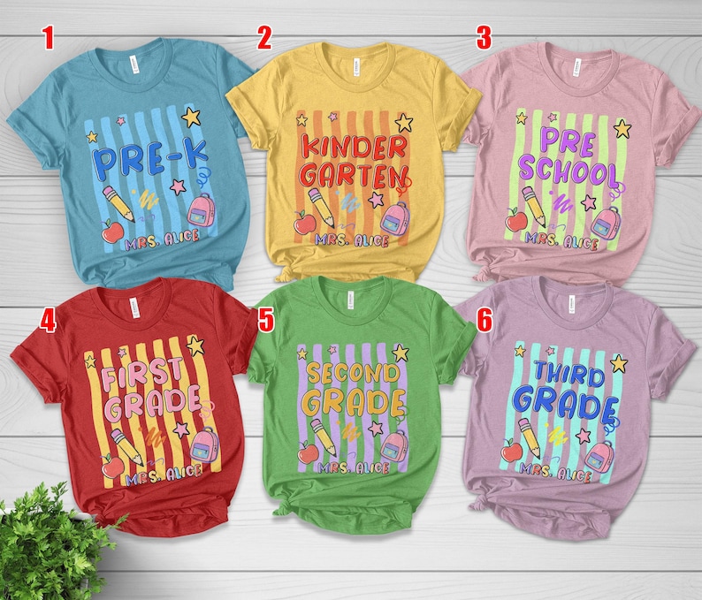 May include: Six colorful t-shirts with school-themed designs. Each shirt features a grade level: Pre-K, Kindergarten, Preschool, First Grade, Second Grade, and Third Grade. Designs include pencils, apples, stars, and backpacks.