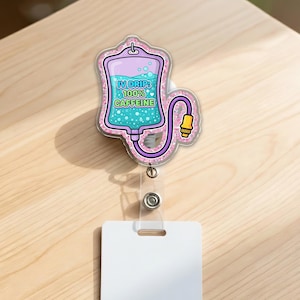 May include: A clear badge reel with a decorative IV drip design. The design features a purple and blue IV bag with the text "IV Drip: 100% Caffeine". The badge reel has a clear plastic strap and a white rectangular card holder.