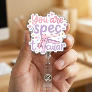 May include: A badge reel with a clear plastic holder and a retractable cord. The badge features the text "You are spectacular" in pink and purple, along with a cartoon illustration of a medical instrument.