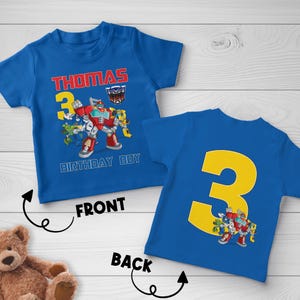May include: Blue short-sleeved t-shirt with a colorful graphic of a robot and the text "THOMAS 3 BIRTHDAY BOY". The back of the shirt features a large yellow number 3 and a smaller robot graphic.