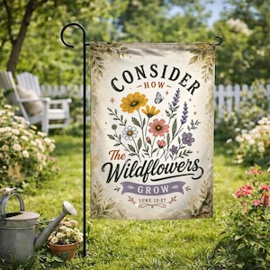 May include: A garden flag with the text "Consider How The Wildflowers Grow" and a floral design. The flag features yellow, pink, white, and purple flowers, with a butterfly and the Bible verse Luke 12:27.