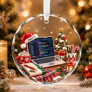 May include: A round, faceted glass Christmas ornament featuring a laptop with code on the screen, a red Santa hat labeled Henry, a notebook, a red mug with whipped cream, a small Christmas tree, and a gift box, with the year 2026 printed.