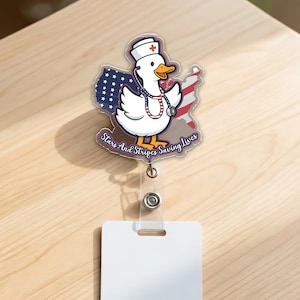 May include: A badge reel featuring a cartoon duck wearing a nurse's hat and stethoscope, with the American flag as a backdrop. The text "Stars And Stripes Saving Lives" is displayed on the badge.
