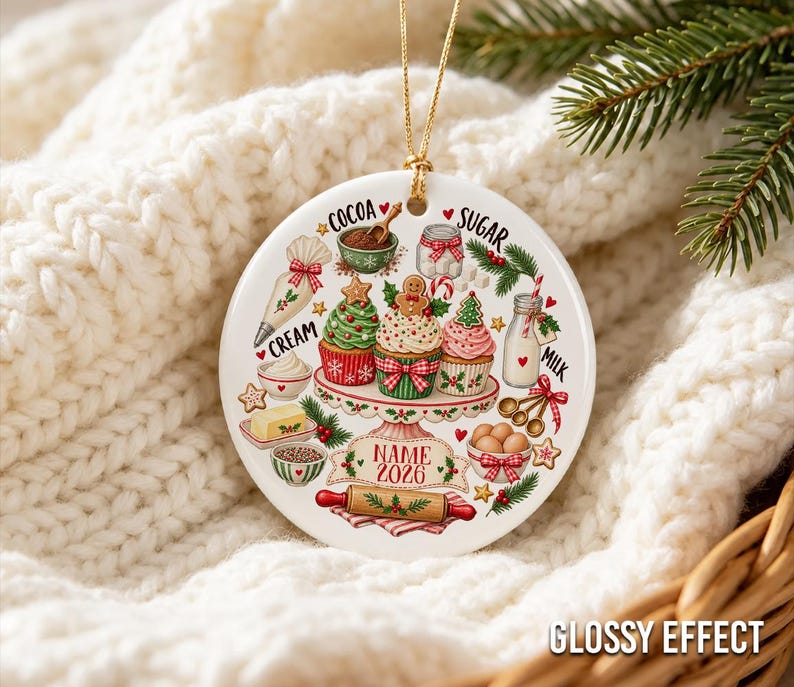 Pu&ograve; includere: Un ornamento rotondo in ceramica bianca con illustrazioni colorate di ingredienti da forno e cupcake su un'alzata. Il design include le scritte COCOA, SUGAR, CREAM, MILK e un nastro con il testo segnaposto NAME 2026.