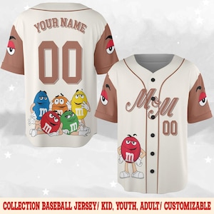 May include: Cream-colored baseball jersey with brown sleeves and accents. The jersey features the text "YOUR NAME" and the number "00" on the back. The front displays the "M&M" logo and the number "00". Cartoon M&M characters are also featured.
