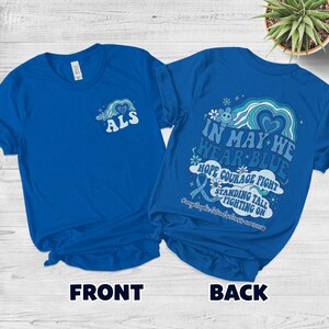 May include: Two royal blue t-shirts. The front shirt has the letters "ALS" with a heart and flower design. The back shirt has the text "IN MAY WE WEAR BLUE" with a ribbon and flower design. The text "HOPE COURAGE FIGHT" is also visible.