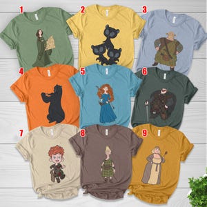 May include: Assorted t-shirts featuring cartoon characters from the movie Brave. The shirts are in various colors, including green, yellow, blue, orange, tan, and brown. Each shirt has a different character design, including Merida, bears, and other characters.