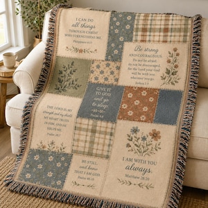 May include: A woven throw blanket featuring a patchwork design with beige, blue, and green panels. The blanket displays floral patterns, plaid squares, and various religious scripture verses printed in black text, finished with a fringed edge.