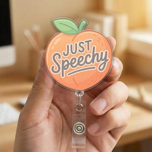 May include: A badge reel with a peach design and the words "JUST Speechy" in a playful font. The peach is orange with a green leaf. The reel has a clear plastic clip and a retractable cord.