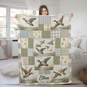 May include: A patchwork quilt featuring mallard ducks in flight over a marshy landscape, interspersed with light blue and sage green gingham and plaid fabric squares. The bottom section includes a rectangular label with the name Ethan.