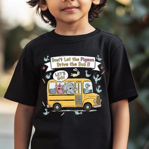 May include: Black t-shirt featuring a yellow school bus with cartoon animals inside and around it. The text "Don't Let the Pigeon Drive the Bus !!" and "LET'S GO!" are also displayed on the shirt. The shirt is worn by a child.