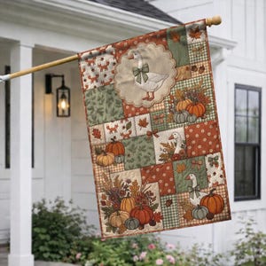 May include: A rectangular garden flag featuring a patchwork design with autumn themes. The pattern includes white geese wearing green plaid bows, orange pumpkins, brown acorns, and small foxes. The color palette consists of orange, green, and tan.