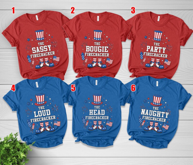 May include: Red and blue t-shirts with patriotic designs. Each shirt features a firecracker theme with text like "Sassy," "Bougie," "Party," "Loud," "Head," and "Naughty." The designs include a top hat, fireworks, and American flags.