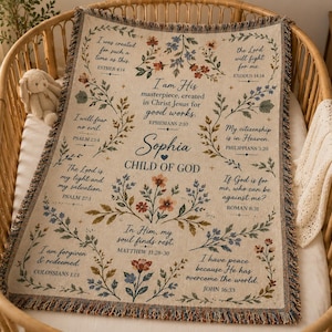 May include: A cream-colored woven throw blanket featuring a fringe edge, floral illustrations, and religious text including the name Sophia, Child of God, and various Bible verses such as Esther 4:14, Ephesians 2:10, and Psalm 23:4.