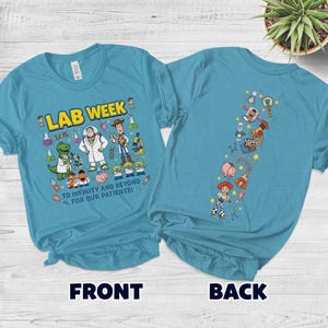 May include: Two light blue t-shirts with a graphic design. The front shirt says "LAB WEEK" with cartoon characters and the text "TO INFINITY AND BEYOND FOR OUR PATIENTS!". The back shirt has a vertical design of cartoon characters.