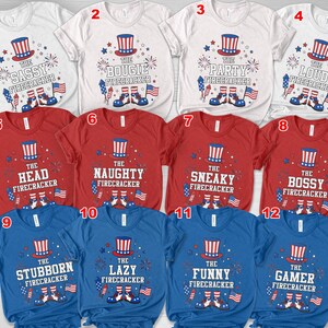 May include: Twelve short-sleeved t-shirts in white, red, and blue, each with a patriotic design. The shirts display an Uncle Sam hat, fireworks, and the phrases "The Sassy Firecracker", "The Bougie Firecracker", "The Party Firecracker", "The Loud Firecracker", "The Head Firecracker", "The Naughty Firecracker", "The Sneaky Firecracker", "The Bossy Firecracker", "The Stubborn Firecracker", "The Lazy Firecracker", "The Funny Firecracker", and "The Gamer Firecracker".