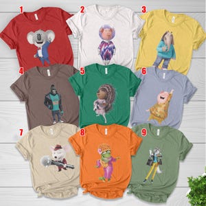 May include: A collection of nine colorful t-shirts featuring characters from the animated movie "Sing." Each shirt displays a different character in a unique design. The shirts are in various colors, including red, white, yellow, brown, green, and orange.